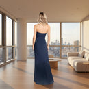 A woman viewed from the back wearing a strapless navy maxi dress against a plain white background.