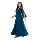 A woman modeling a floor-length teal blue dress with a V-neckline, flared elbow-length sleeves, a fitted waist, and a front slit, shown against a plain white background.