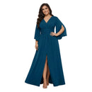 A woman modeling a floor-length teal blue gown with a V-neckline, flared elbow-length sleeves, a matching waist tie, and a high front slit, shown against a plain white background.