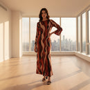 A woman modeling a long-sleeved maxi dress with an abstract wavy stripe pattern in red, black, and beige, set against a plain white background.