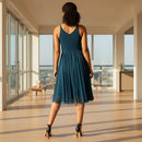 A woman modeling a sleeveless V-neck midi dress with a pleated skirt and tulle hem, shown from the back against a plain white background.