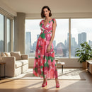 A woman modeling a vibrant pink, red, and green floral print midi dress with a wrap-style bodice and tie-shoulder straps, set against a plain white background.