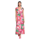 A woman modeling a sleeveless maxi dress with a vibrant pink, green, and white abstract floral pattern against a solid white background.
