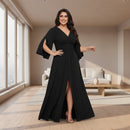 A woman modeling a floor-length black gown with a V-neckline, draped cap sleeves, a gathered waist, and a high front slit, photographed against a plain white background.