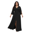 A woman modeling a long black maxi dress with a V-neckline, elbow-length sleeves, side slit details, and a high front slit, shown against a plain white background.