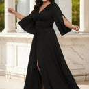 A woman wearing a floor-length black gown with a V-neckline, flared elbow-length sleeves, a fitted waist, and a high front slit, posed in front of a white marble colonnade.