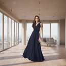 A woman modeling a floor-length navy blue gown with a V-neckline, ruffled shoulder details, and a flowing skirt, set against a plain white background.