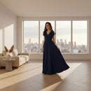 A woman modeling a navy blue floor-length maxi dress with flutter sleeves and a V-neckline, shown against a plain white background.