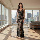 A woman modeling a floor-length black lace gown with a shimmering metallic gold floral pattern, set against a plain white background.