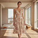 A woman modeling a sleeveless V-neck midi dress with a beige mesh base and white floral lace applique, paired with nude high-heeled sandals against a plain white background.