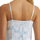 Close-up back view of a woman wearing a white camisole-style top with thin shoulder straps and a smocked center back panel, featuring a light blue scenic print.