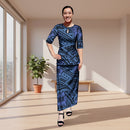 A woman modeling a two-piece matching set featuring a short-sleeve top and a long maxi skirt, both printed with a Polynesian tribal pattern in shades of blue, purple, and black. She is wearing black strappy high-heeled sandals against a solid white background.